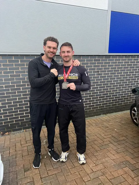 Two jiu-jitsu athletes outside a competition venue, one wearing a medal