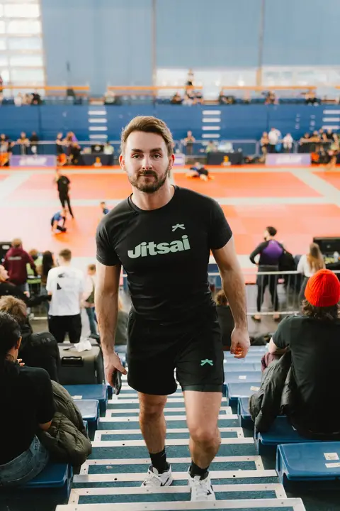 A man in a JitsAI T-shirt walking down the stands at a jiu-jitsu tournament
