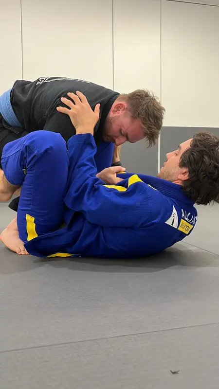 Two people training jiu-jitsu on the mat, one in a blue gi