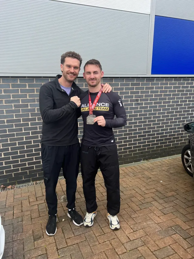 Two jiu-jitsu athletes outside a competition venue, one wearing a medal