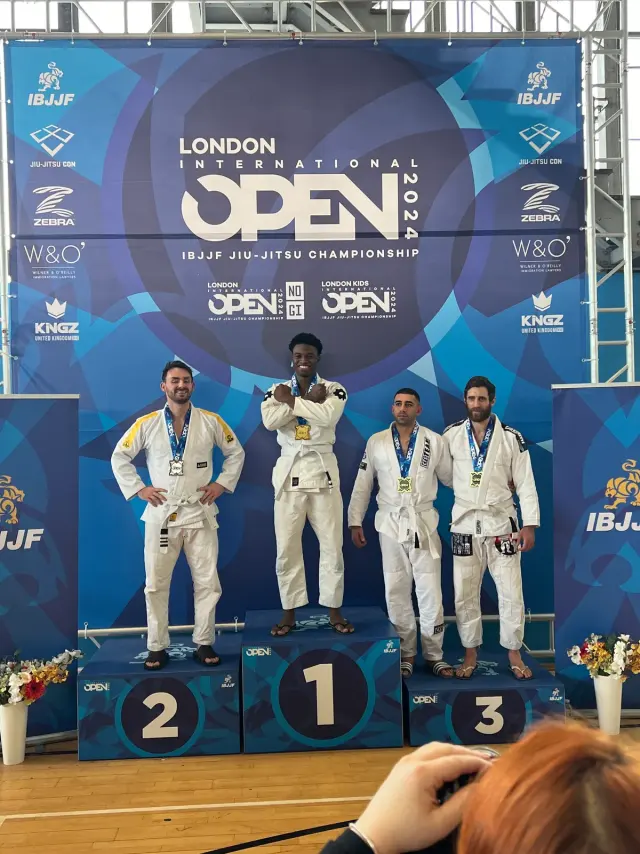 Four jiu-jitsu athletes in white gis with their medals on the podium at the IBJJF London International Open